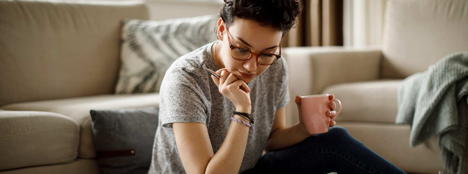 Woman in living room looking down and holding coffee.