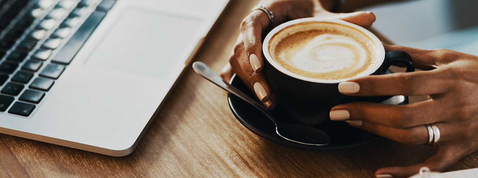 two hands holding a cup of coffee next to an open laptop